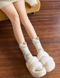 Close-up of cozy coral fleece cat socks with fluffy cream slippers on wooden floor