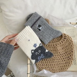 Gros plan de chaussettes en laine Fair Isle grises avec chat tricoté et broderie fleurie