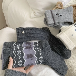 Détail de chaussettes en laine Fair Isle grises avec broderie chat sur fond blanc