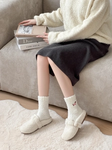 Close-up of white plush slippers and fleece socks featuring delicate pink embroidery