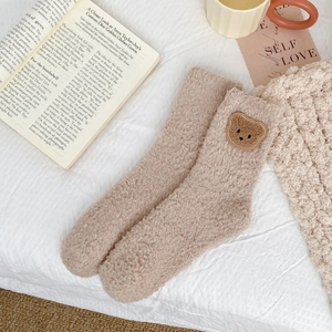Close-up of khaki coral fleece socks with cute bear embroidery in a cozy home setting
