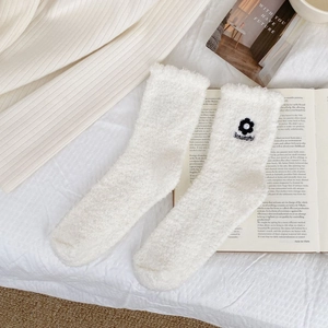 Detail of white coral fleece sock featuring a black flower embroidery and pearl accents