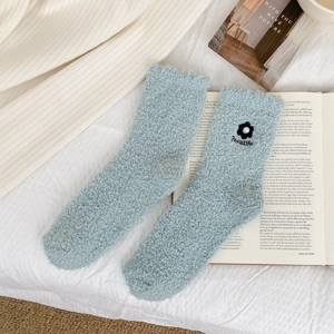 Detail of coral fleece sock in mint green with embroidered flower and pearl on a book
