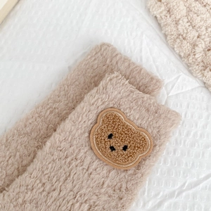 Close-up of fluffy coral fleece winter socks featuring a cute brown bear embroidery