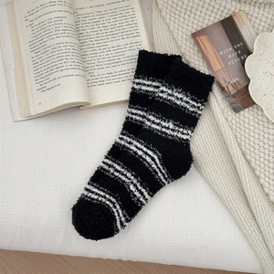 Detail of soft coral fleece striped socks on cozy knitted blanket with book décor