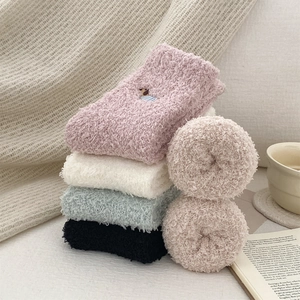 Detail showing plush coral fleece socks with cute bear embroidery and soft winter colors
