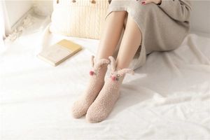 Detail of coral fleece slipper socks featuring cute plush rabbit ears and 3D pom pom nose