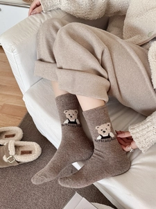 Détail de chaussettes en laine marron chaud avec écusson ours en peluche et texture douce