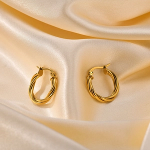Detail of golden twisted hoop earrings on cream silk fabric with spring clasp mechanism