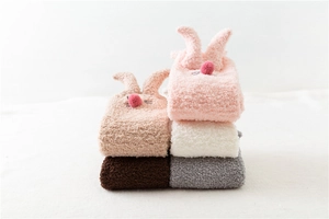 Close-up of soft coral fleece slipper socks with cute rabbit ears and 3D plush ball details