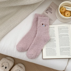 Detail of pink coral fleece winter socks with dog embroidery on a cozy knitted blanket