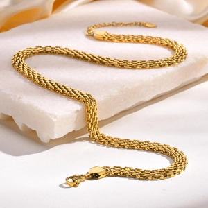 Gros plan d'un collier en maille tressée dorée à trois rangs sur socle en marbre
