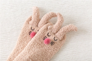 Close-up of coral fleece rabbit socks with pink pom-pom nose and cute 3D ears