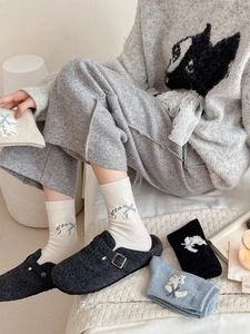 Détail de chaussettes en laine épaisses à motif chat portées avec des mules grises élégantes