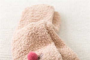 Macro shot of soft coral fleece material with plush pink pom-poms and fine embroidery