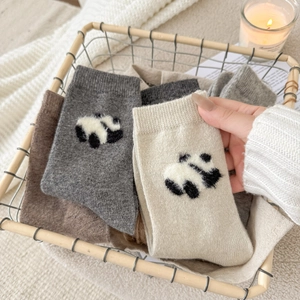 Dettaglio di calze di lana invernali con ricamo a forma di panda in diversi colori neutri