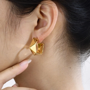 Close-up of modern golden geometric C-shaped hoop earrings worn on an ear for style