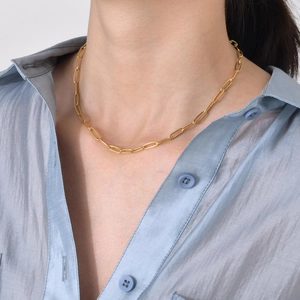 Close-up of a golden paperclip link chain necklace worn on a light blue textured shirt