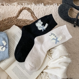 Détail de chaussettes en laine avec broderie chat et nœud posées sur un livre