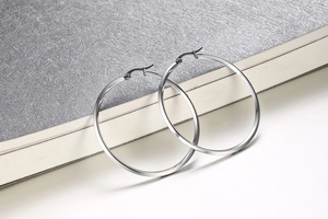 Close-up of polished silver hoop earrings leaning on a book in a minimalist studio setting