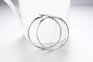 Detailed view of large polished silver hoop earrings resting on white ceramic