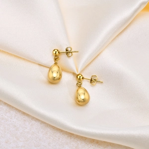 Detailed view of polished golden teardrop earrings on elegant cream satin fabric
