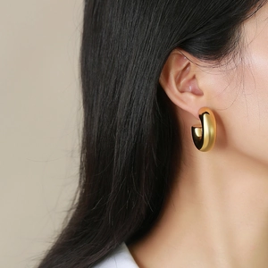 Gros plan d'une boucle d'oreille créole dorée épaisse en forme de C sur un mannequin