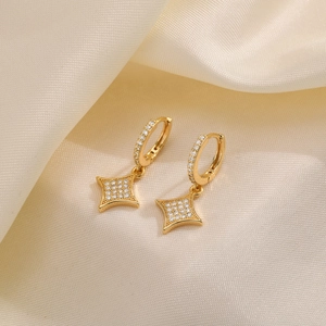 Macro shot of gold star hoop earrings with sparkling cubic zirconia on cream satin