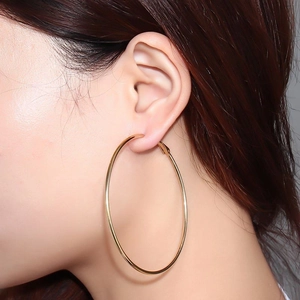 Grandes boucles d'oreilles créoles dorées en acier inoxydable poli portées par un mannequin
