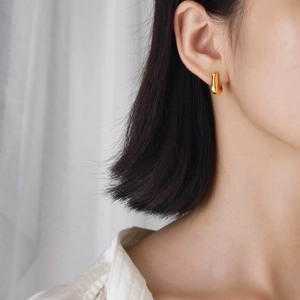 Boucle d'oreille géométrique en U dorée portée par un mannequin sur fond de tissu doux