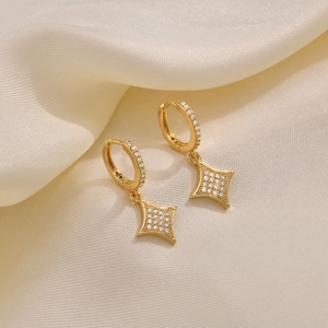 Macro shot of gold four-pointed star earrings with micro-set zircon on silk fabric