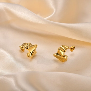 Détail de boucles d'oreilles dorées en forme de C texturées sur du satin de soie