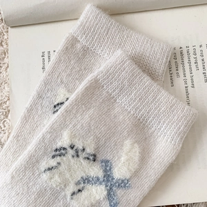 Détail de chaussettes en laine avec broderie chat pelucheuse et motifs croisés bleus