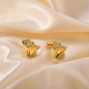 Vue macro de boucles d'oreilles dorées irrégulières en C sur fond de soie champagne