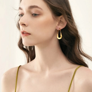 Close-up of golden mobius twist hoop earrings worn by a model to show style