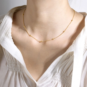 Vue rapprochée d'un collier chaîne serpent à perles dorées sur une chemise blanche