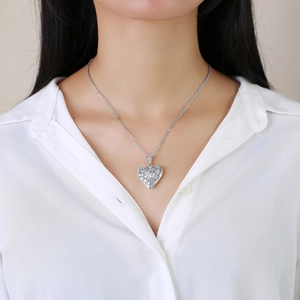 Close-up of silver hollow heart locket necklace worn on neck with white shirt background