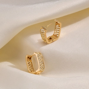 Detail of gold-plated U-shaped earrings with white zircon pavé on beige silk fabric