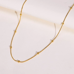 Détail d'un collier chaîne serpent dorée avec perles d'espacement sur socle blanc