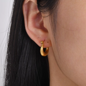 Gros plan d'une boucle d'oreille créole minimaliste creuse en titane or 18 carats sur modèle