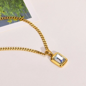Macro view of gold curb chain necklace featuring emerald cut white zircon pendant