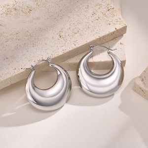 Détail de boucles d'oreilles épaisses en forme de goutte argentée sur socle beige