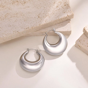 Gros plan de boucles d'oreilles créoles argentées sur un support en pierre