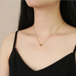 Close-up of a textured gold bead pendant on a minimalist chain worn by a model