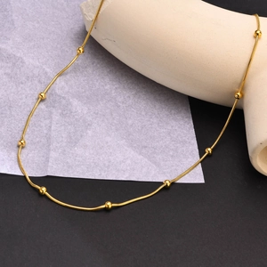 Détail d'un collier à chaîne serpent dorée avec perles sur des supports géométriques
