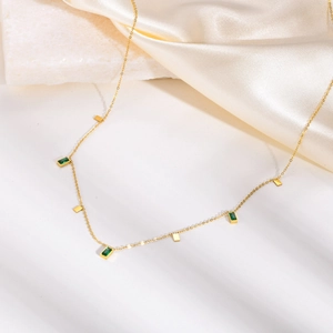 Close-up of golden necklace with green rectangular stones on white silk and marble