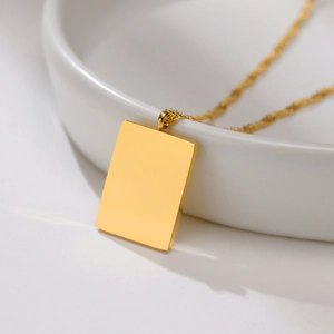 Close-up of polished gold rectangular pendant with fine twisted wave chain on white ceramic