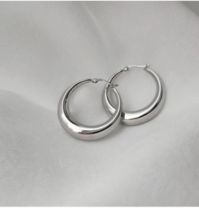 Vue détaillée de boucles d'oreilles créoles argentées polies sur tissu de soie blanc