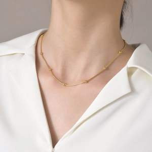 Détail d'un collier chaîne serpent dorée avec billes polies porté sur une chemise