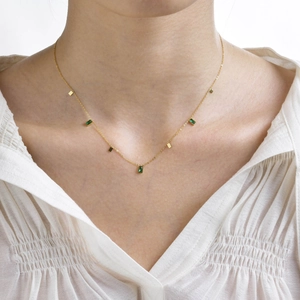 Close-up of gold collar necklace with green rectangular zircon stones on a model
